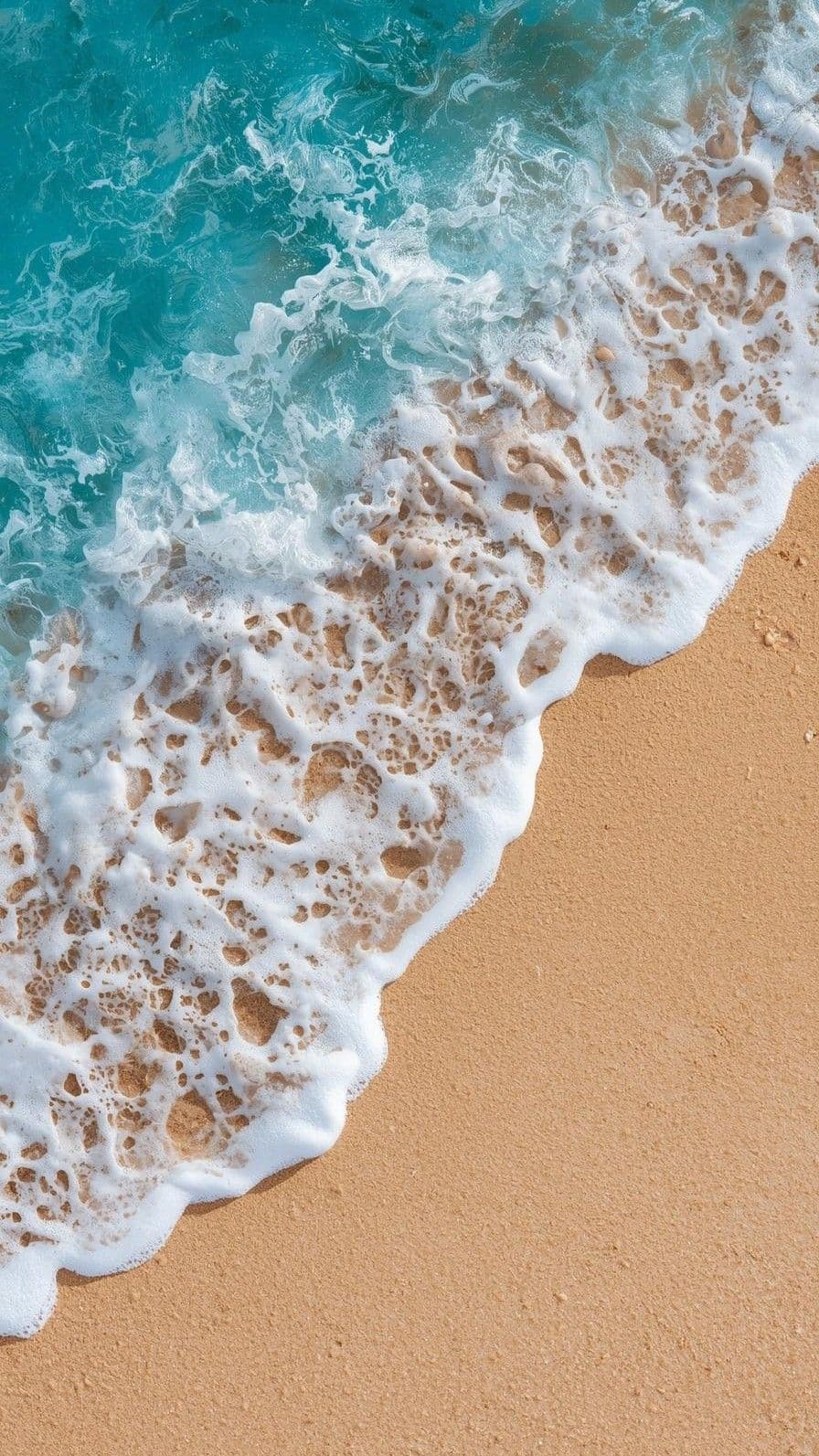 This image captures a serene coastal scene from a high-angle perspective, showcasing the dynamic interaction between turquoise ocean waves and golden sand. The waves, frothy with white foam, crash gently onto the shore, revealing intricate patterns of bubbles and textures as they recede. The sand appears fine-grained and sunlit, contrasting beautifully with the vibrant blue water. The composition emphasizes natural beauty and tranquility, with no human presence or stylized elements. The lighting is bright and even, suggesting a clear, sunny day, enhancing the vividness of the colors and the peaceful atmosphere. The overall mood is calming and meditative, evoking a sense of relaxation and connection with nature.