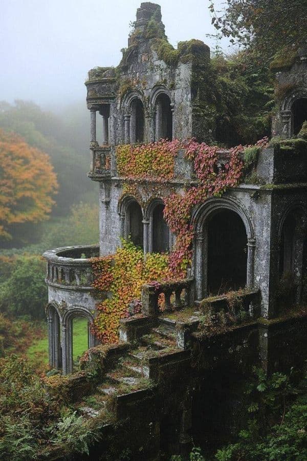 The image depicts a grand, weathered stone mansion in ruins, its architecture featuring arched windows, ornate balconies, and crumbling staircases, all enveloped by lush, overgrown vegetation. Vibrant autumnal ivy in shades of red, orange, and yellow cascades down the stone walls, contrasting with the moss-covered surfaces and the misty, foggy atmosphere. The setting is a misty, forested hillside with trees displaying fall colors, suggesting a serene, abandoned, and nature-reclaiming environment. The photograph employs a cinematic composition with soft, diffused lighting, emphasizing textures and depth, creating a melancholic yet peaceful mood. The overall aesthetic is one of quiet decay and natural beauty, evoking nostalgia and mystery through its atmospheric perspective and detailed architectural decay.