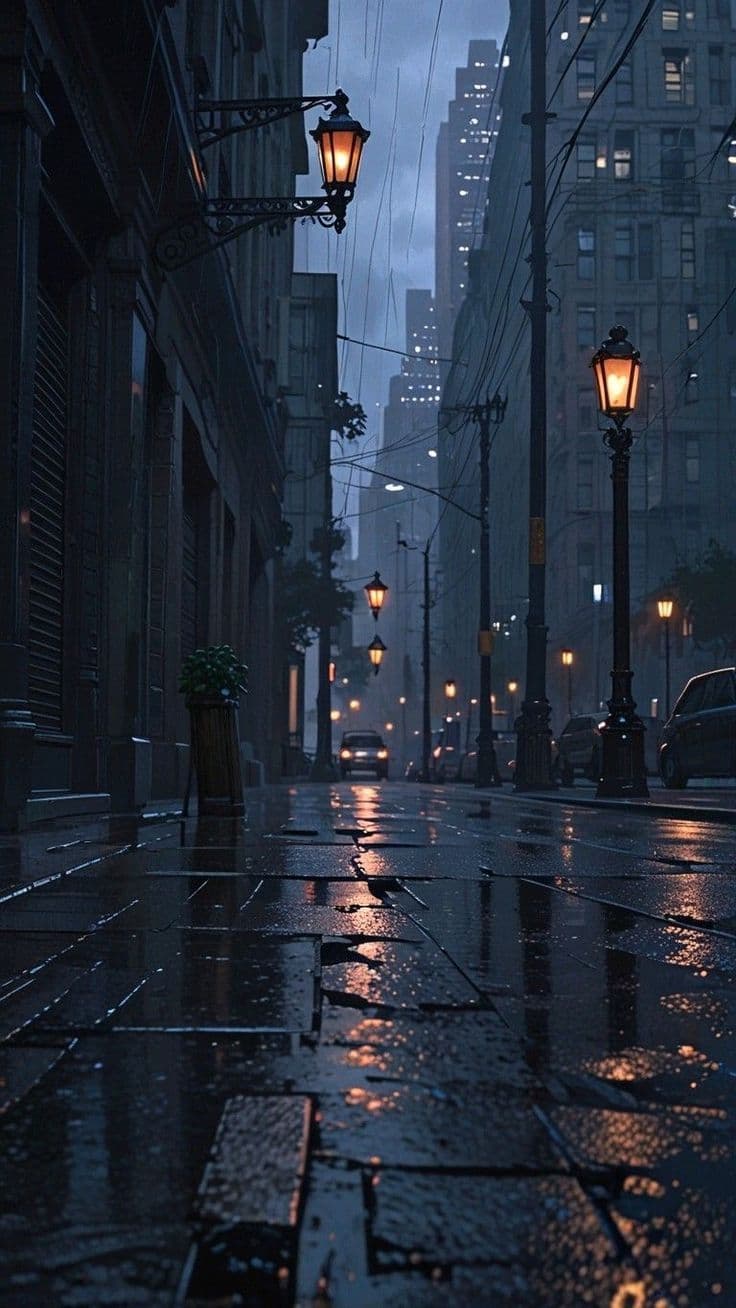 The image captures a moody, atmospheric urban street scene at dusk, with wet cobblestones reflecting the warm glow of vintage street lamps. Tall, shadowy buildings line both sides of the alley, their facades partially obscured by mist and rain. A solitary car is visible in the distance, its headlights piercing the gloom, while overhead wires and lampposts create a sense of depth and urban density. The composition uses a low-angle perspective to emphasize the reflective pavement and the towering architecture, evoking a quiet, contemplative mood. The lighting is soft and diffused, with a cool blue-gray palette contrasted by the amber light from the lamps, enhancing the scene's cinematic and melancholic tone.