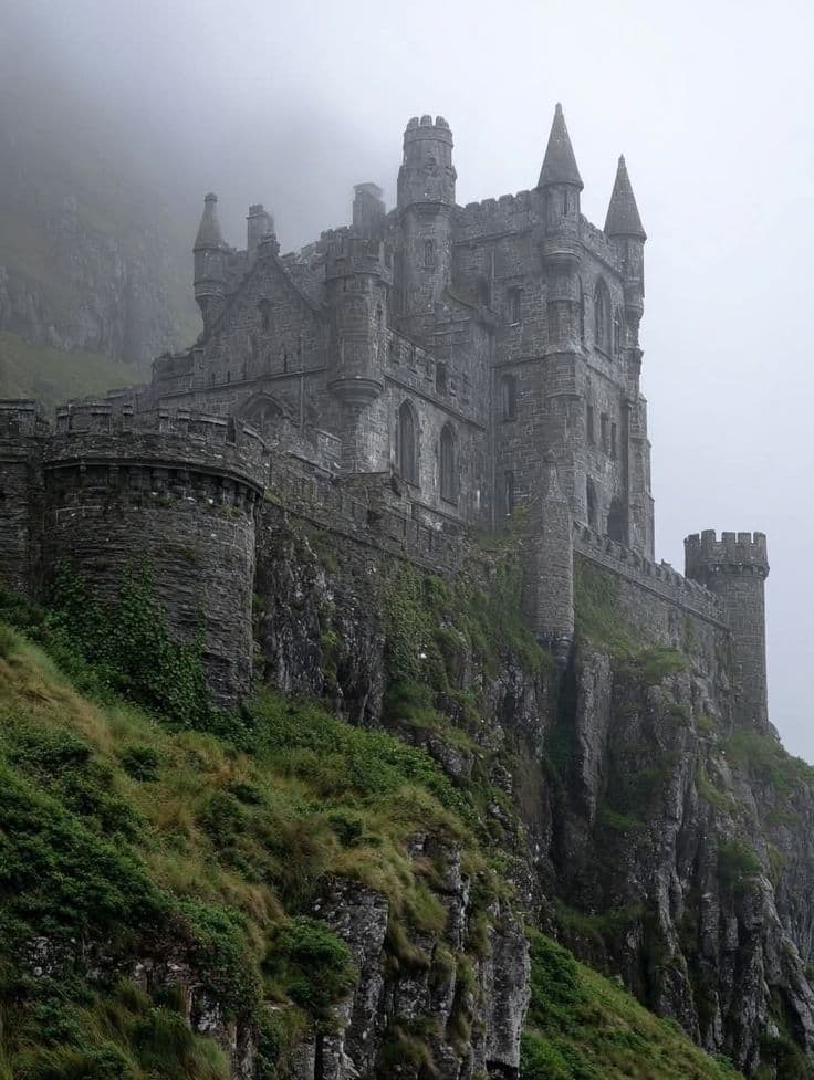 The image features a grand, ancient stone castle perched precariously on a steep, mist-covered cliffside, its multiple turrets and battlements rising against a pale, foggy sky. The structure exhibits Gothic architectural elements with arched windows and crenellated walls, suggesting a medieval or fantasy setting. The surrounding landscape is lush with green moss and grass clinging to the rocky terrain, enhancing the castle's imposing and isolated presence. The atmosphere is moody and atmospheric, with soft, diffused lighting from an overcast day, creating a sense of mystery and timelessness. The composition emphasizes the castle's scale and the dramatic interplay between its solid stone form and the ethereal fog enveloping its upper sections.