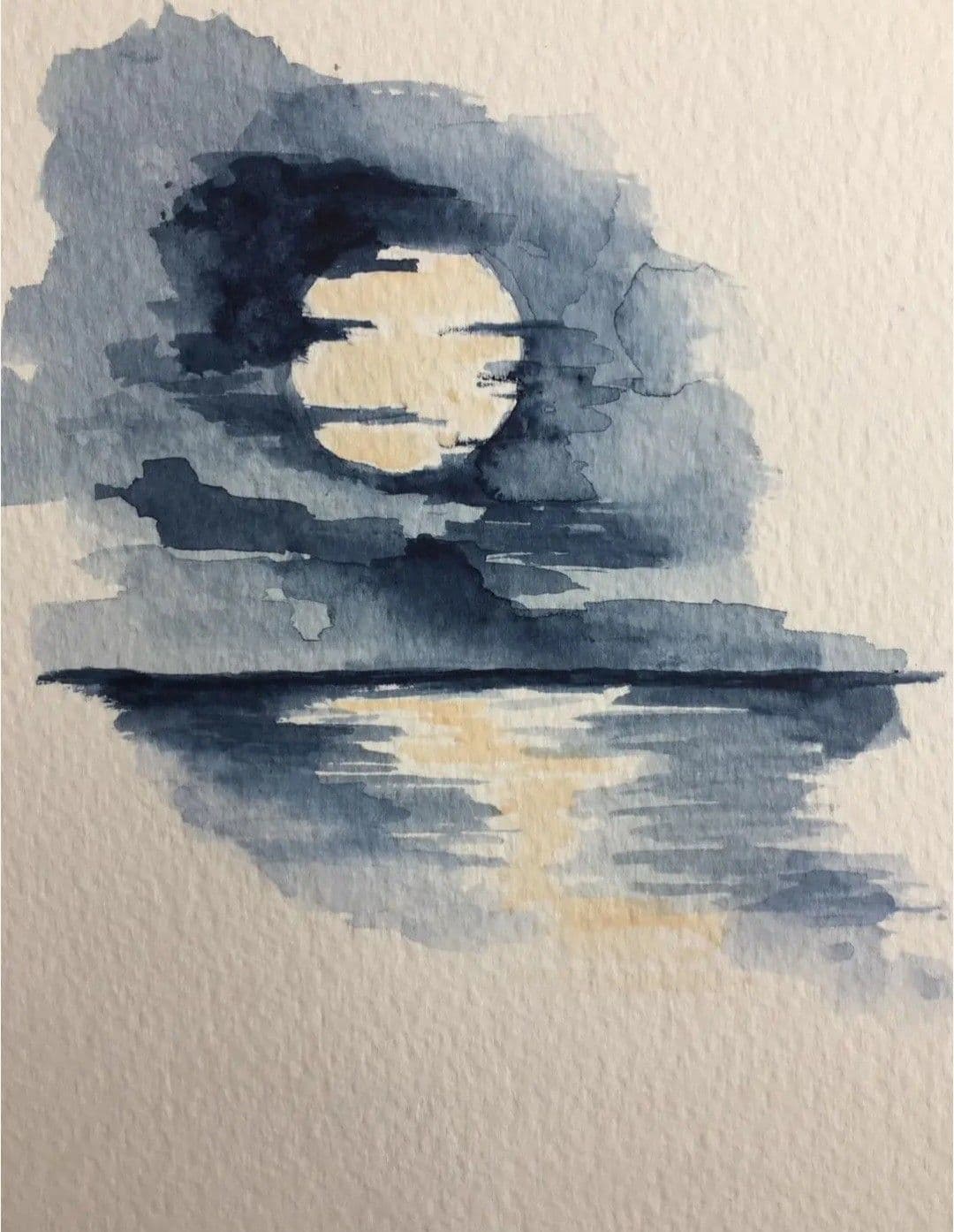 This watercolor artwork depicts a serene nocturnal scene featuring a luminous full moon partially obscured by dark, textured clouds. The moon's reflection shimmers across a calm body of water, rendered with soft, wavy brushstrokes that suggest gentle ripples. The composition is minimalist, emphasizing the interplay of light and shadow, with the moon serving as the central focal point. The artist employs a cool color palette dominated by deep blues and grays, accented by a warm, pale yellow glow from the moon, creating a tranquil and contemplative atmosphere. The texture of the watercolor paper is visible, adding a tactile, organic quality to the piece, which enhances its peaceful, meditative mood.