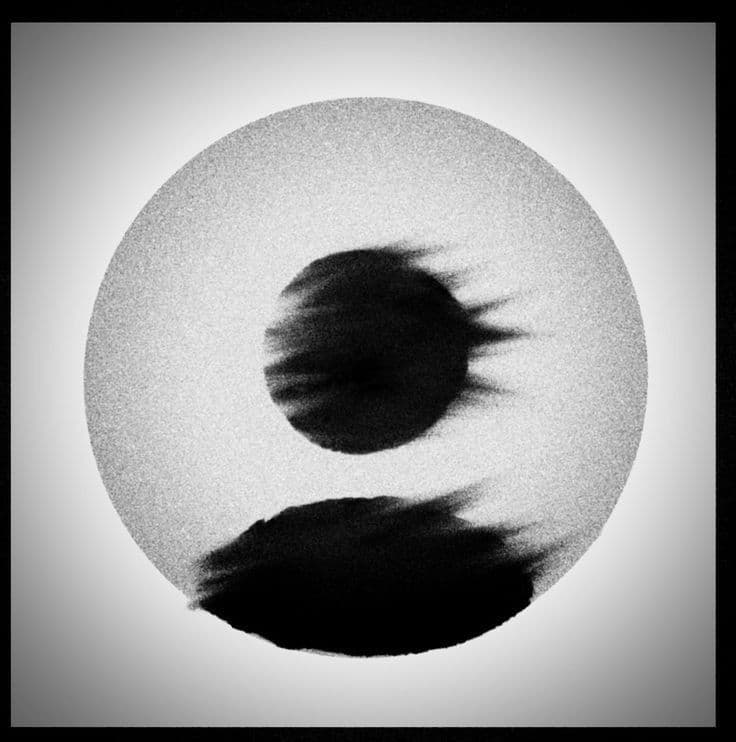The image presents a minimalist abstract composition centered on a circular frame with a textured, grainy grayscale background. Within the circle, two distinct, blurred black forms resembling stylized eyes or orbs are positioned—one upper, one lower—creating a sense of duality or balance. The forms exhibit soft, painterly brushstrokes with visible texture, suggesting an ink or watercolor medium. The overall aesthetic is serene and contemplative, evoking themes of introspection or cosmic balance. The image is framed by a subtle vignette, enhancing its focus on the central abstract elements. The composition is symmetrical and meditative, inviting quiet observation.