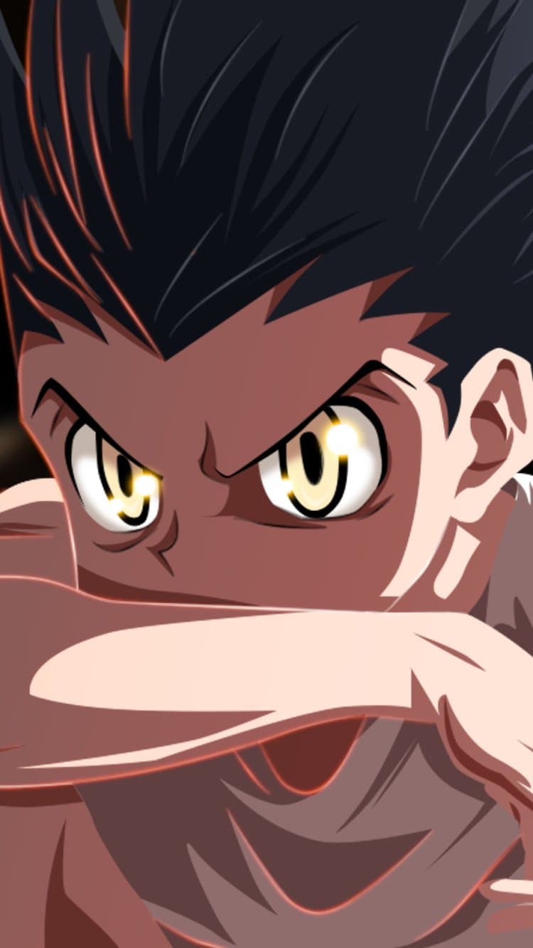 The image features a close-up, intense portrait of Gon Freecss, the protagonist of Hunter x Hunter, during a moment of extreme focus. He is depicted with his signature spiky black hair and large, glowing amber eyes that serve as the primary focal point. His arm is raised across the lower half of his face in a defensive or preparatory combat stance, showing only his eyes and forehead. The artistic style utilizes sharp cel-shading with high-contrast shadows and bright highlights to emphasize the dramatic tension. The background is dark and indistinct, pushing all visual weight onto the character's determined expression. The overall atmosphere is one of high emotional intensity, power, and unwavering resolve.